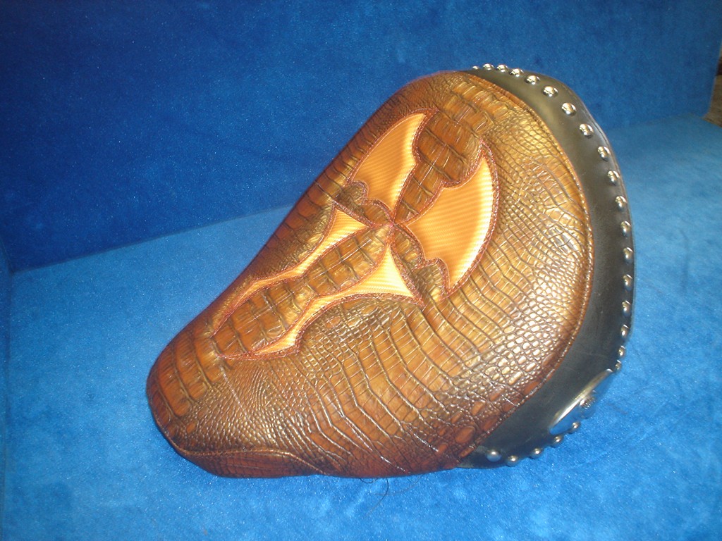 Solo seat in copper-toned gator with a tooled cross and studded edge
